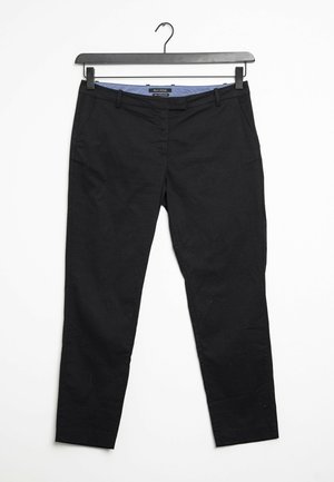 Pantalones negros de corte recto colgados en una percha negra, con trabillas para cinturón y bolsillos laterales, sobre un fondo blanco.