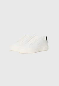 White sneakers with a smooth texture, featuring a black heel accent, round toe, and flat white sole. Laced design and logo on side.