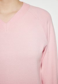 Rosa gestrickter Pullover mit V-Ausschnitt, geripptem Halsausschnitt und Raglanärmeln, mit einer weichen Textur und gleichmäßiger Farbausgabe.
