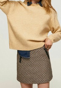 Maglione beige con orlo a costine, abbinato a una gonna a fantasia con linee diagonali marroni, nere e crema e dettagli in denim sulle tasche.