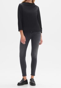 Maglione nero, con texture, a collo barca e maniche a tre quarti, abbinato a jeans skinny grigio scuro e mocassini neri.