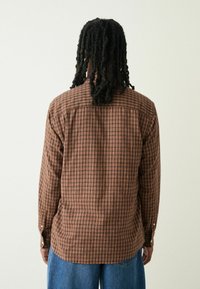 Braun und orange kariertes Hemd mit Rückenpasse und geknöpften Manschetten. Aus gewobenem Stoff gefertigt, mit lockerer Passform und langen Ärmeln.