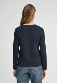 Granatowa, długorękawowa koszulka z okrągłym dekoltem, wykonana z bawełnianej tkaniny o gładkiej fakturze i luźnym kroju. Noszona z jasnoniebieskimi dżinsami.