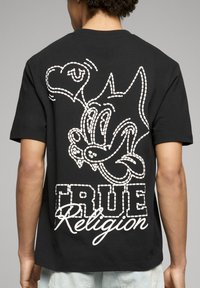 T-shirt nera in cotone con grafica a contorno bianca di un personaggio e la scritta "TRUE Religion" sul retro. Maniche corte, vestibilità comoda.
