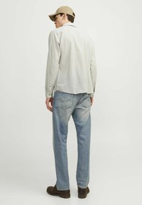 Camicia a maniche lunghe a righe grigio chiaro con una vestibilità rilassata, abbinata a jeans blu sbiaditi e scarpe marroni, completata da un cappellino beige.