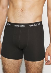 Schwarze Baumwollstretch-Boxershorts mit einem markierten Bund. Sie bieten eine enge Passform und eine glatte Textur, die für Komfort und Unterstützung konzipiert ist.