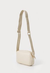 Sac bandoulière beige avec une texture lisse, de forme rectangulaire, fermoir doré et une bandoulière en toile avec une personnalisation.