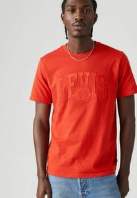 Rode katoenen T-shirt met reliëflogo "LEVI'S" in het midden, ronde hals, korte mouwen en een relaxte pasvorm, gecombineerd met blauwe denim shorts.