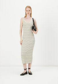 Bežinė ir juoda dryžuota midi suknelė, pagaminta iš minkštos medžiagos. Modelis laiko mažą juodą rankinę ir dėvi juodas plokščias batus.