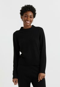Pull en tricot noir avec un col et un ourlet côtelés. Manches longues, texture douce, design ajusté, associé à un pantalon assorti.