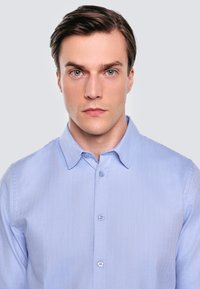 Jasnoniebieska koszula z długim rękawem w wzór jodełki, klasyczny kołnierzyk i delikatny połysk. Posiada slim fit oraz pasujące guziki.