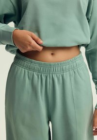 Jasnozielona bluza z luźnym krojem i ściągaczami, w komplecie z dopasowanymi spodniami z elastycznym pasem o gładkiej fakturze.