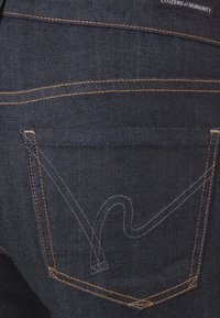 Ciemnoniebieskie dżinsy z denimu z tylną kieszenią, która ma haftowane detale, w tym zakrzywiony wzór i miedziane nici.