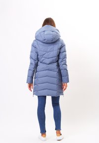 Puffjacka i ljusblått med huva, med en vadderad design, långa ärmar och sidodragkedjor. Kombinerad med blå jeans och vita skor.