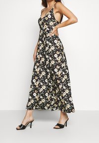 Kwiatowa sukienka midi w kolorze czarnym z białymi, żółtymi i zielonymi kwiatami. Posiada głęboki dekolt, cienkie ramiączka oraz luźny krój.