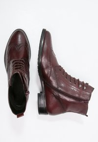 Botas de tobillo de cuero burdeos con punta redonda, cordones en la parte delantera, detalle de cremallera y un acabado texturizado. Suelas de cuero planas con un ligero tacón.