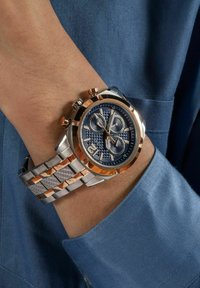 Orologio cronografo argento e oro rosa con quadrante blu, motivi texturizzati, tre sub-quadranti e bracciale in metallo misto al polso.