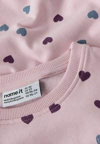 Maglione di cotone rosa chiaro con motivo a cuori piccoli viola e blu su tutta la superficie, con scollo a girocollo a coste e etichetta di cura visibile.