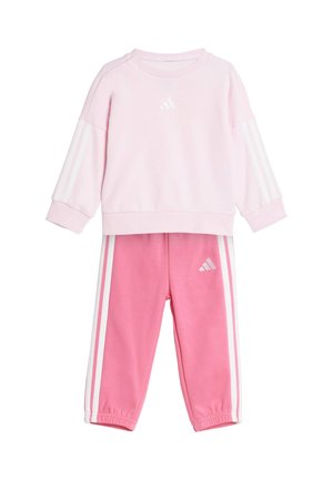 Sweatshirt rose avec des rayures blanches et un logo, associé à un pantalon rose avec des rayures blanches sur les côtés. Tissu doux, coupe décontractée, encolure ras du cou.