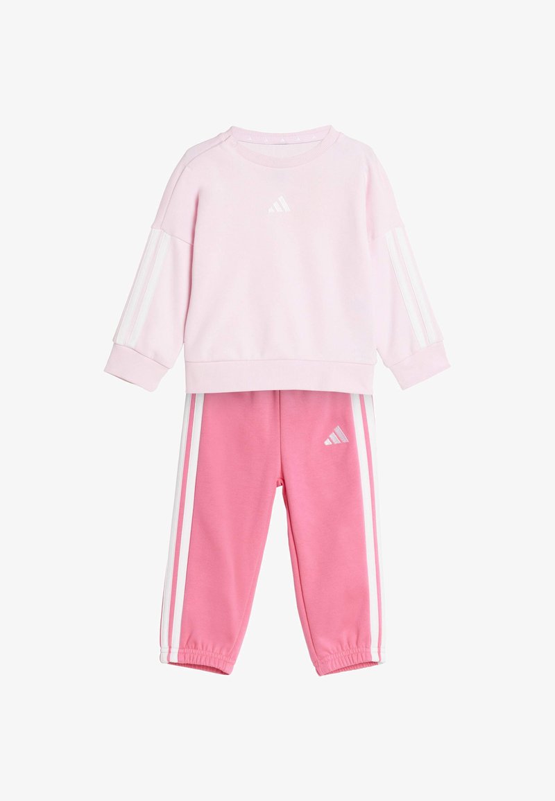 Ružová mikina s bielymi pruhmi a logom, skombinovaná s ružovými nohavicami s bielymi bočnými pruhmi. Mäkko tkanina, uvoľnený strih, okrúhly výstrih.