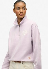 Jasnofioletowy polarowy sweatshirt na zamek błyskawiczny z wysokim kołnierzem i haftowanym logo. Posiada długie rękawy i metkę z logo marki.