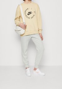 Nike-tröja i ljusgult med grafiskt tryck, kombinerad med ljusgrå joggers och vita sneakers med en rosa detalj. Vit handväska.