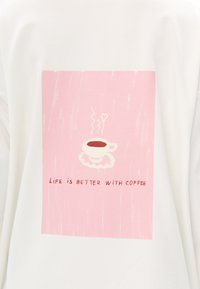 Weißer Sweatshirt mit einem rosa rechteckigen Motiv. Es zeigt eine dampfende Kaffeetasse auf einer weißen Untertasse mit dem Text „Das Leben ist besser mit Kaffee.“