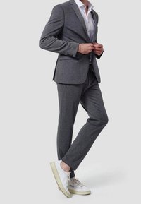 Gray, fitted suit with a textured fabric, featuring a single-breasted jacket and slim trousers. Paired with white sneakers for a casual look.