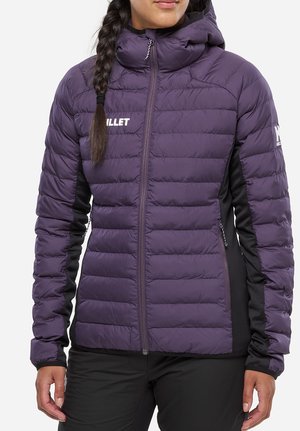 Femme portant une veste matelassée violette avec des panneaux latéraux noirs, une fermeture éclair à l'avant et un col montant, avec une tresse sur une épaule.