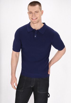 Kurzärmeliges navy Polohemd mit einem strukturierten Rautenmuster, Knopfleiste und geripptem Kragen, kombiniert mit dunklen Denim-Hosen.