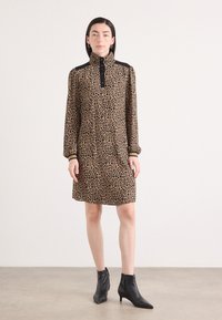 Leopardenmuster-Kleid mit hohem Kragen, langen Ärmeln und Knopfdetails. Schwarze Akzente an den Schultern, kombiniert mit schwarzen Knöchelstiefeln.