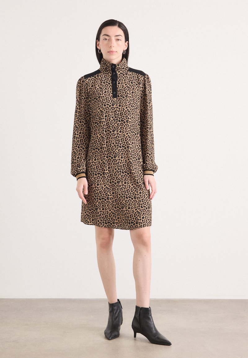 Leopardenmuster-Kleid mit hohem Kragen, langen Ärmeln und Knopfdetails. Schwarze Akzente an den Schultern, kombiniert mit schwarzen Knöchelstiefeln.