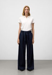 Vit kortärmad pikétröja med krage, kombinerad med mörkblå, höga vida byxor med en knytbälte. Slät textur.