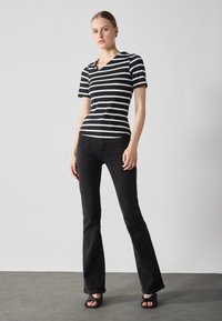 Black and white striped short-sleeve top with a v-neck, paired with black flared jeans and black strappy sandals. Smooth fabric textures.