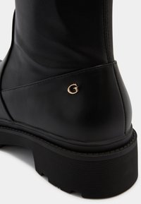 Bottine en cuir noir avec dessus texturé, semelle en caoutchouc épaisse et un accent de logo "G" doré sur le côté.