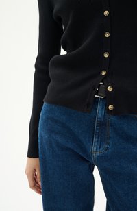 Svart räfflad cardigan med guldknappar, matchad med blå denimjeans. Fokusera på knappar, textur av tyget och plaggets passform.