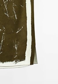 Tissu marron avec une bordure irrégulière blanc cassé et des traits blancs abstraits, présentant un bord plié en couches sur un fond blanc uni.