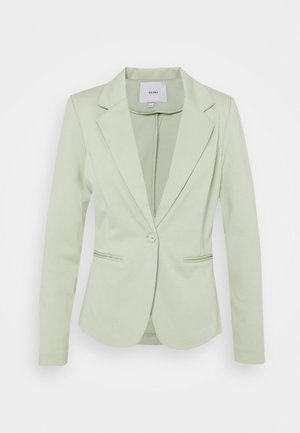 Blazer femenino verde claro a medida con solapas con muesca, cierre con un solo botón, mangas largas y dos bolsillos frontales con abertura.