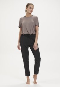 Brun t-shirt med kort ärm som kombineras med svarta joggbyxor med elastisk midja och snörning. Slät textur; avslappnad passform.