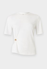 T-shirt blanc en tissu doux, avec des manches courtes et un design torsadé à la taille agrémenté d'un détail circulaire doré.