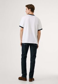 Λευκό κοντομάνικο πουκάμισο με ναυτική ρίγα, ελαφρύ ύφασμα, απεικονίζεται από πίσω. Συνδυάζεται με σκούρα μπλε τζην παντελόνι και καφέ παπούτσια.