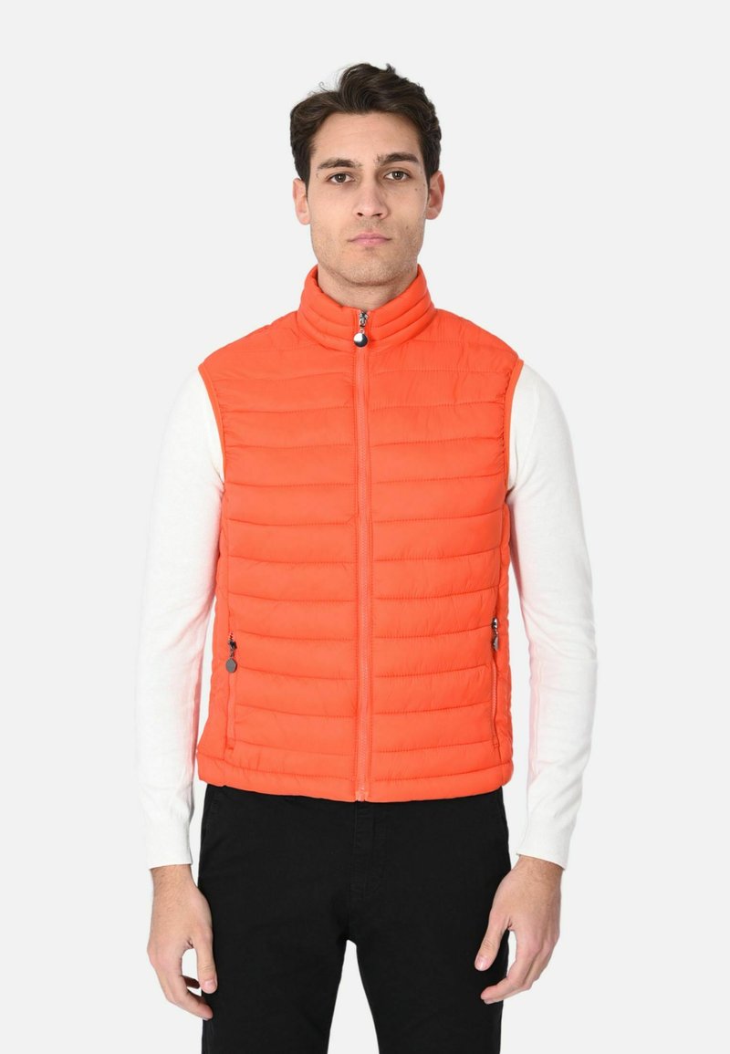Gilet arancione imbottito con colletto alto, chiusura con zip e tasche laterali, indossato sopra una camicia bianca a maniche lunghe, abbinato a pantaloni neri.
