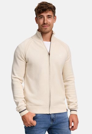 Kremfarget zip-up genser med teksturert overflate, raglanermed og stripete mansjetter. Kombinert med blå jeans, som viser en avslappet stil.