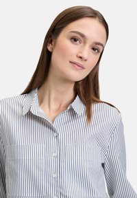 Striped button-up shirt in blue and white, featuring a collar, two front pockets, and a lightweight, smooth fabric texture.