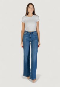 Hvid ribbet kortærmet top parret med højtaljede blå vide jeans, der har en klassisk denimstruktur og et understated design.