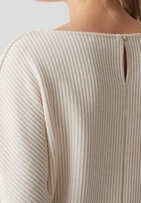 Top a righe beige con texture a coste, dotato di un'apertura a chiave sulla schiena chiusa da un bottone. Design semplice e leggero.