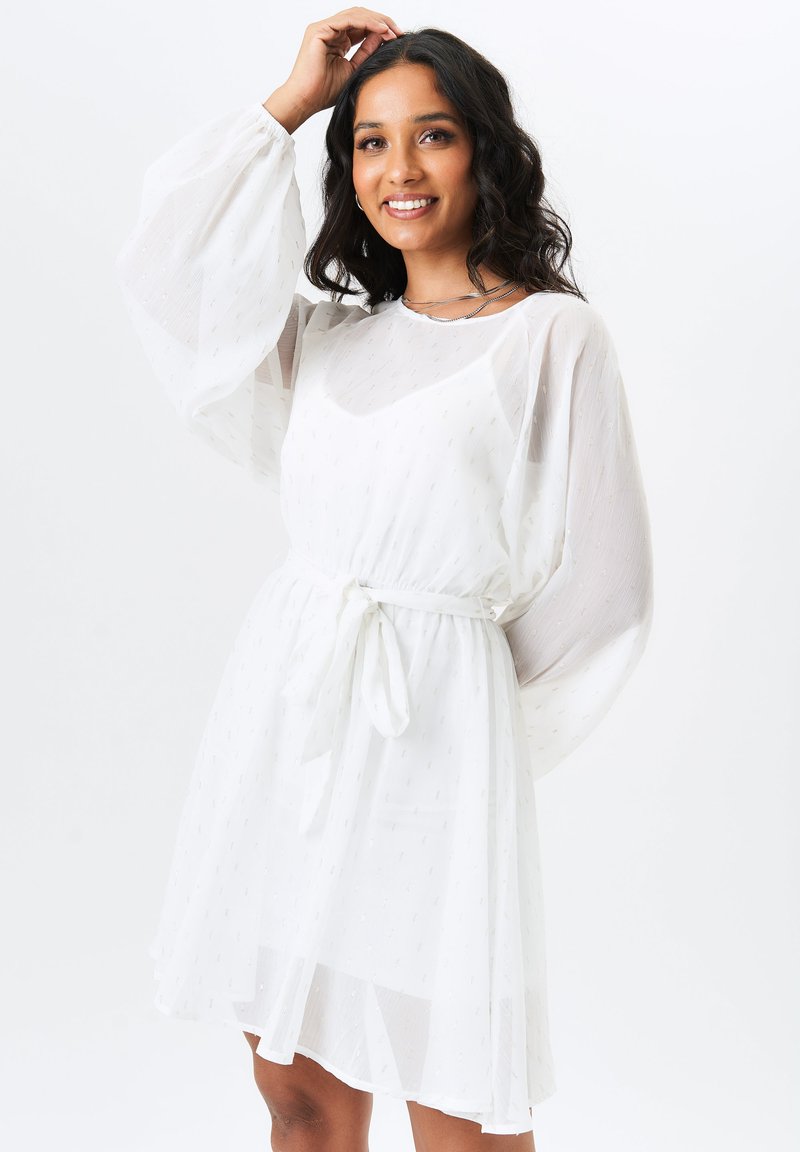 White dress made of sheer fabric with a tie waist. It features long, puffed sleeves and a textured pattern throughout.