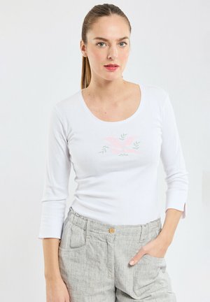 T-shirt blanc à manches longues avec un col rond et un motif floral en rose doux et vert, associé à un pantalon en lin gris clair avec des poches.