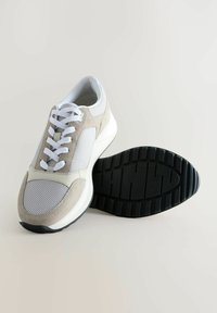 Leichter Sneaker mit einem Obermaterial aus hellgrauem Wildleder und Mesh, weißen Schnürsenkeln und einer strukturierten schwarzen Gummisohle mit einem auffälligen Profil.