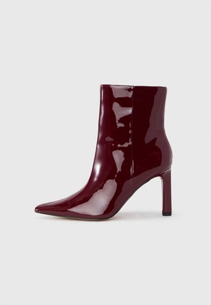Stivaletto alla caviglia in vernice bordeaux lucida con punta appuntita e tacco alto sottile su uno sfondo chiaro uniforme.